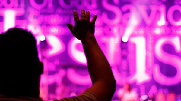 Person holding up hand worshipping in front of a purple lit Jesus banner during Contemporary Services at Saxe Gotha